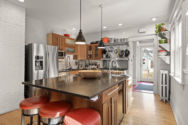 kitchen with dark countertops, radiator heating unit, appliances with stainless steel finishes, light wood-style floors, and brown cabinetry