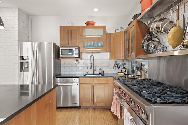 kitchen featuring dark countertops, tasteful backsplash, light wood-style flooring, appliances with stainless steel finishes, and a sink