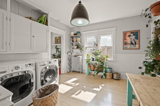 clothes washing area with cabinet space, radiator heating unit, separate washer and dryer, and light wood-type flooring