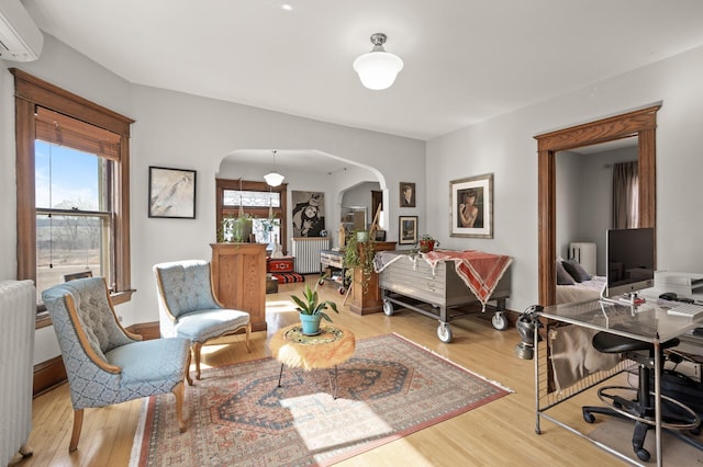 living area featuring arched walkways, radiator, a wall mounted air conditioner, and light wood-type flooring