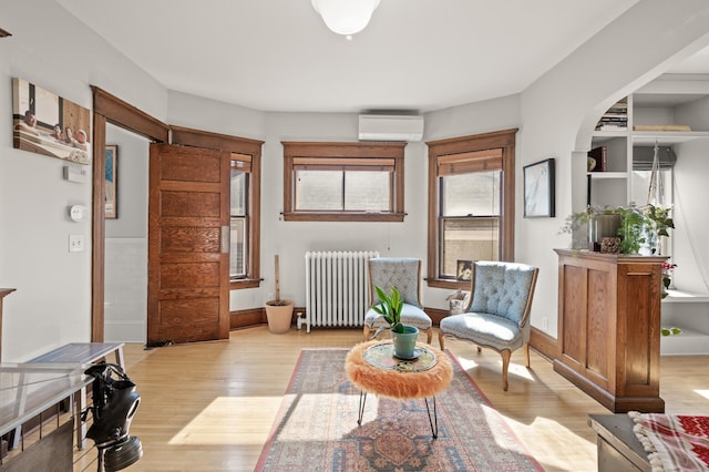 sitting room with light wood finished floors, a wall mounted AC, radiator heating unit, and baseboards