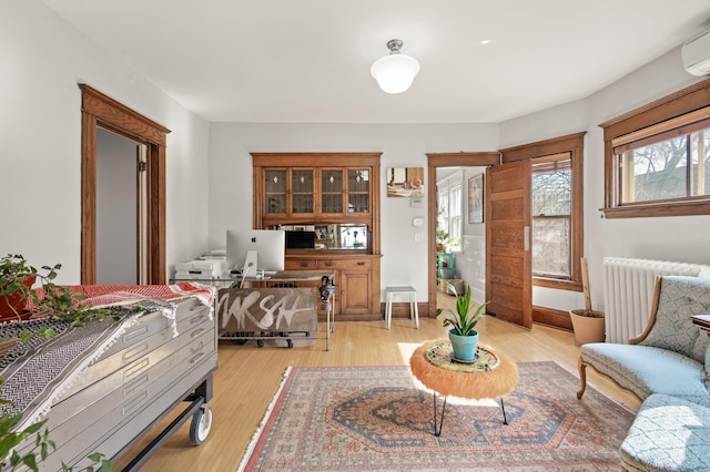 interior space with a wall mounted air conditioner, light wood-type flooring, baseboards, and radiator