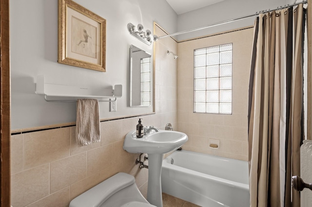 bathroom with shower / bathtub combination with curtain, toilet, tile walls, and a wainscoted wall