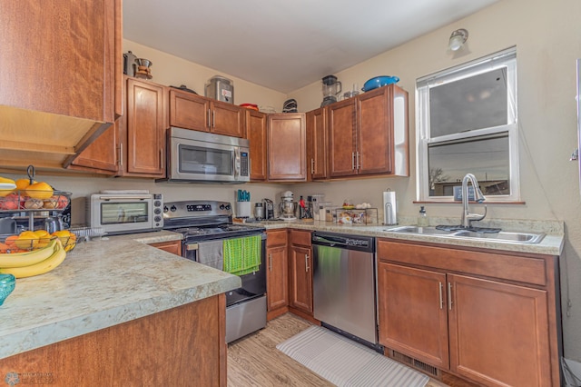 kitchen with light wood-style flooring, a sink, appliances with stainless steel finishes, a toaster, and light countertops