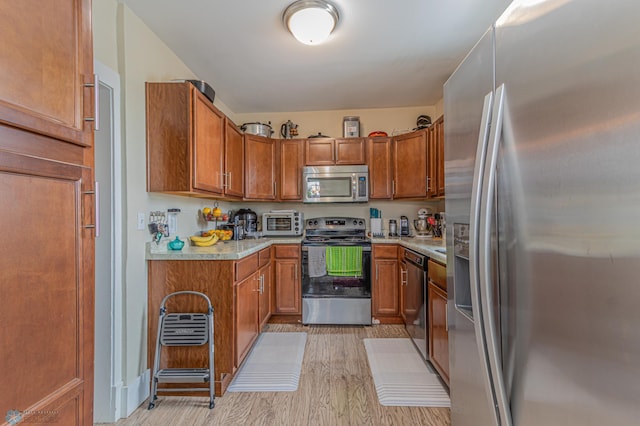 kitchen featuring light wood-type flooring, a toaster, light countertops, appliances with stainless steel finishes, and brown cabinets