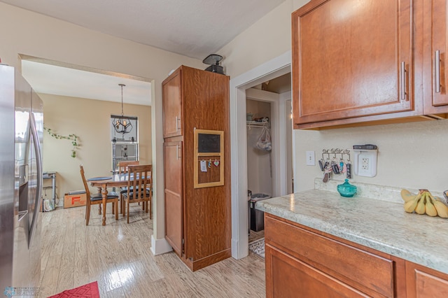 kitchen with hanging light fixtures, light wood-type flooring, stainless steel fridge, and brown cabinets