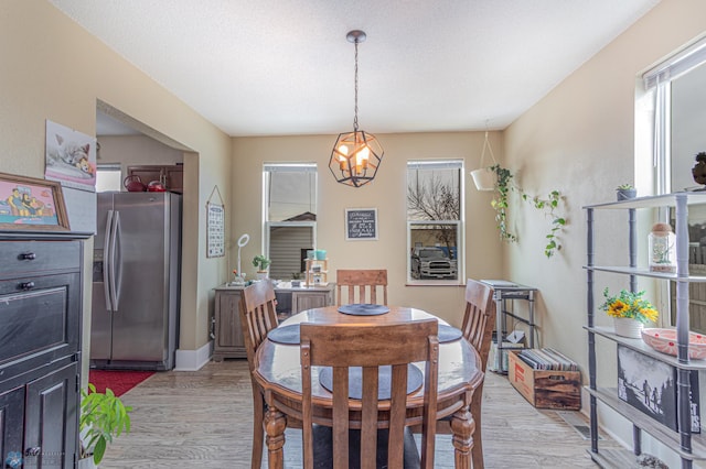 dining room with a notable chandelier, light wood-style floors, baseboards, and a textured ceiling