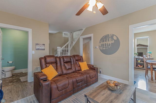 living room featuring stairway, ceiling fan, baseboards, and wood finished floors