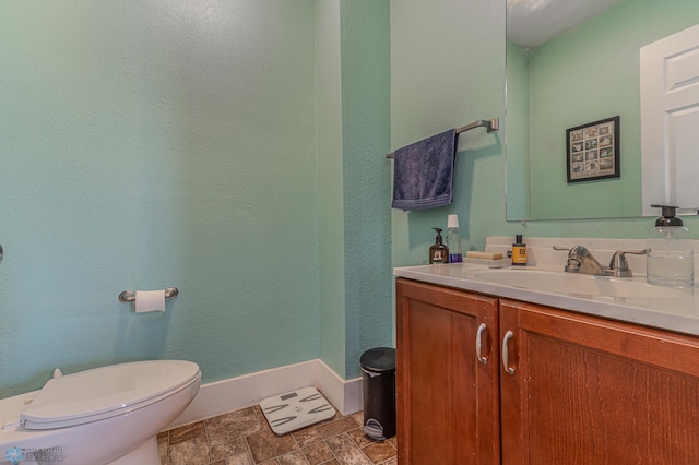 half bath with vanity, stone finish floor, toilet, and baseboards