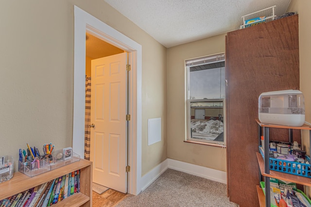 corridor with light carpet, a textured ceiling, and baseboards