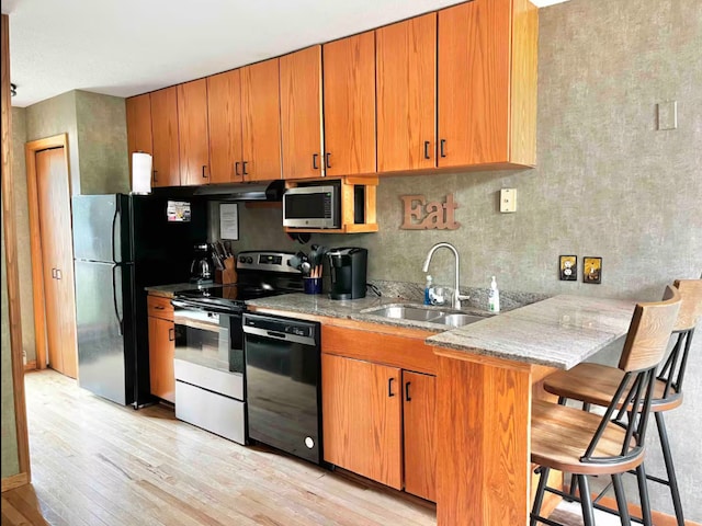 kitchen with light wood-style flooring, a sink, black appliances, light stone countertops, and a kitchen breakfast bar