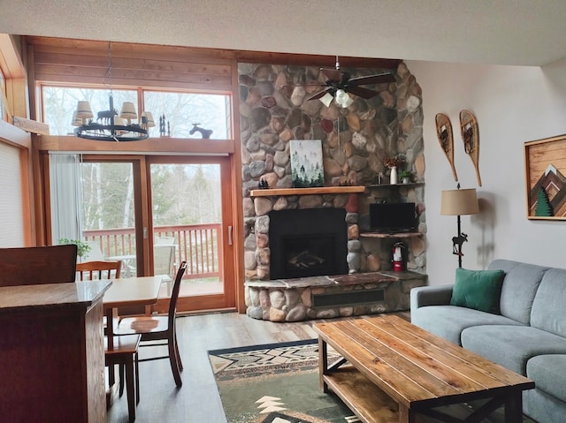 living area with a textured ceiling, a stone fireplace, ceiling fan with notable chandelier, and wood finished floors