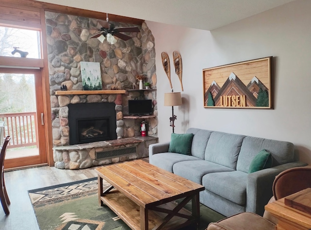 living area featuring ceiling fan, a stone fireplace, and wood finished floors