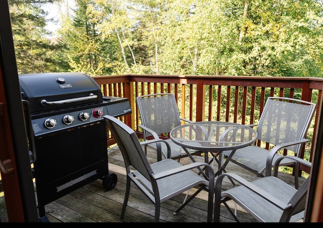 wooden terrace with outdoor dining space, area for grilling, and a view of trees