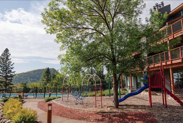 community jungle gym featuring fence, a mountain view, and a community pool