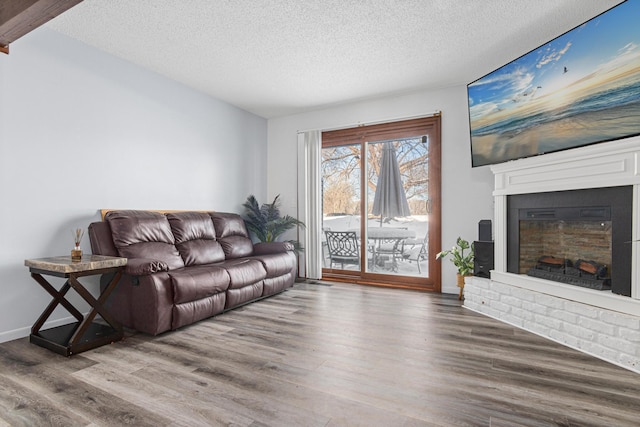 living area featuring a brick fireplace, a textured ceiling, baseboards, and wood finished floors