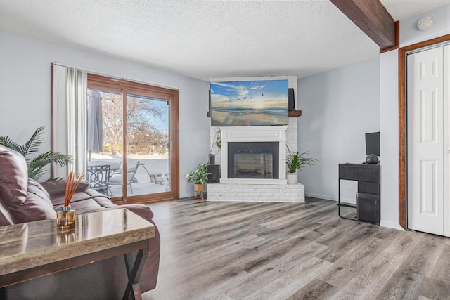 living room featuring a brick fireplace, a textured ceiling, wood finished floors, beamed ceiling, and baseboards