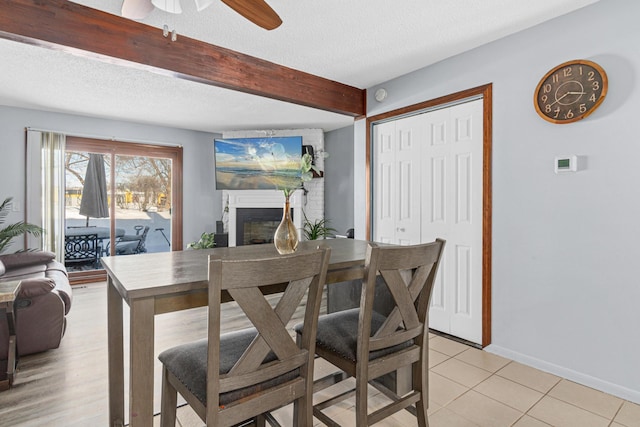 dining space with baseboards, a fireplace, a textured ceiling, and beamed ceiling