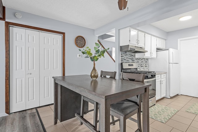 kitchen featuring backsplash, gas stove, white cabinetry, a textured ceiling, and under cabinet range hood