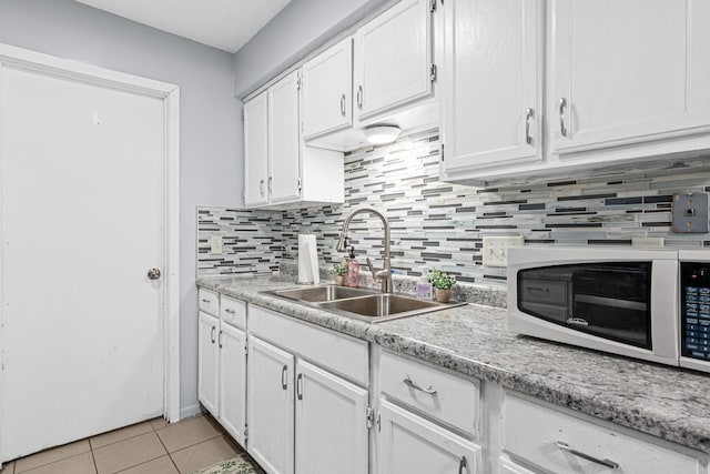 kitchen with white microwave, light tile patterned flooring, a sink, and white cabinetry