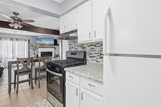 kitchen featuring freestanding refrigerator, stainless steel gas range, under cabinet range hood, a fireplace, and backsplash