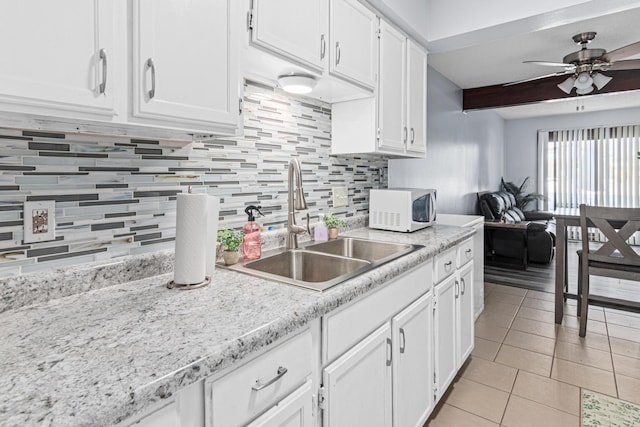 kitchen with light tile patterned floors, white microwave, light countertops, white cabinetry, and a sink