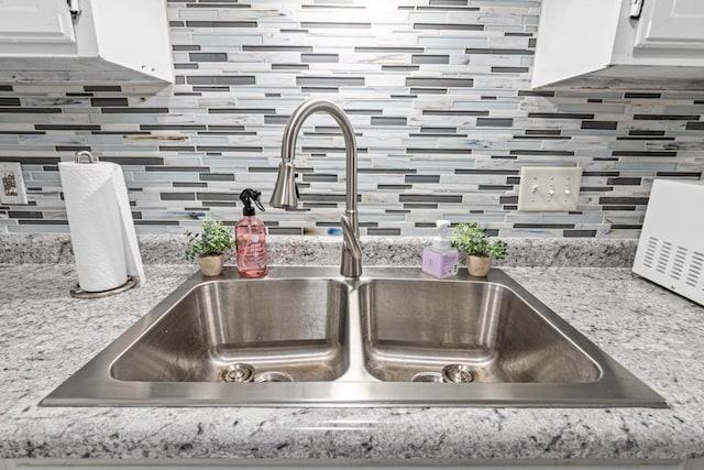 room details featuring tasteful backsplash, a sink, white cabinetry, and light stone countertops