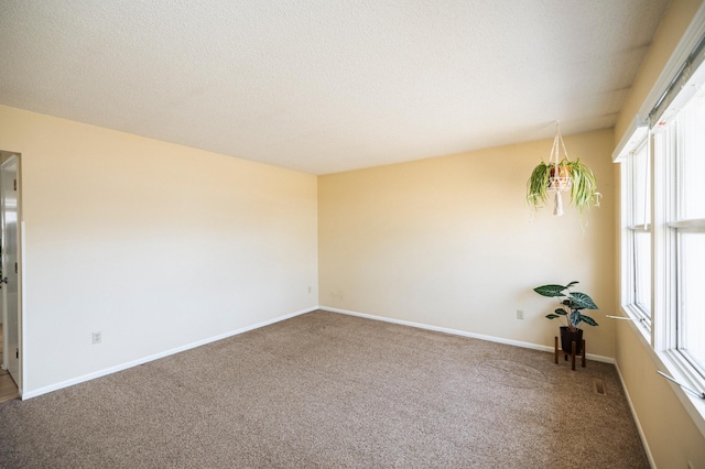 empty room with carpet flooring, baseboards, and a textured ceiling