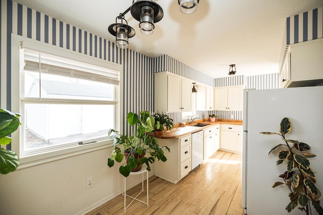 kitchen featuring wooden counters, white appliances, wallpapered walls, and a sink