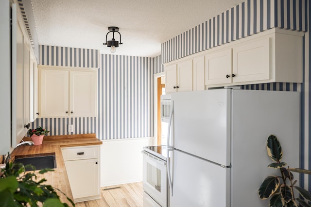 kitchen with wallpapered walls, white appliances, a textured ceiling, and a sink