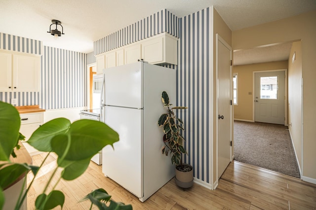 kitchen featuring wallpapered walls, baseboards, light wood-style flooring, freestanding refrigerator, and white cabinets