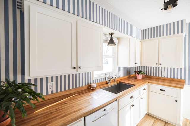 kitchen featuring wallpapered walls, butcher block countertops, white dishwasher, white cabinetry, and a sink