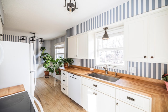 kitchen featuring wallpapered walls, butcher block counters, white appliances, white cabinetry, and a sink