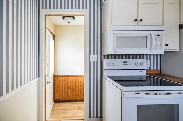 kitchen with white appliances, white cabinets, wainscoting, and wallpapered walls