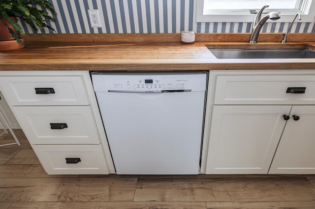 kitchen with wallpapered walls, white dishwasher, a sink, butcher block countertops, and white cabinetry