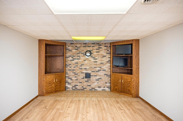 empty room with baseboards, built in shelves, visible vents, and light wood finished floors