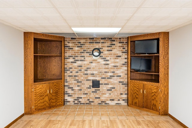 empty room with wood finished floors, baseboards, and brick wall