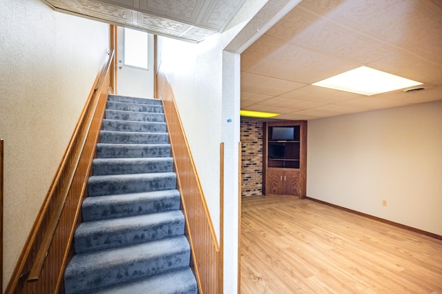 stairway with a paneled ceiling, wood finished floors, visible vents, and baseboards