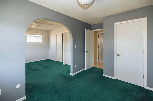 interior space featuring a ceiling fan, carpet, baseboards, arched walkways, and a textured ceiling