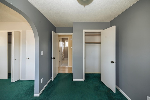 unfurnished bedroom with baseboards, arched walkways, carpet, and a textured ceiling