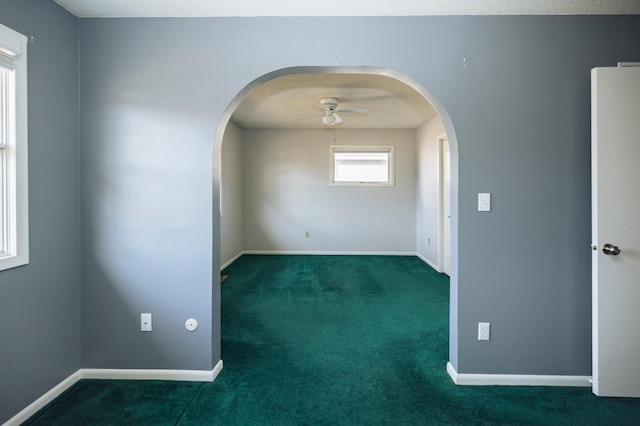 carpeted spare room featuring a textured ceiling, a ceiling fan, arched walkways, and baseboards