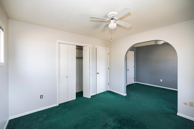 unfurnished bedroom featuring baseboards, arched walkways, a closet, a textured ceiling, and carpet flooring