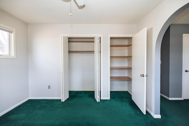 unfurnished bedroom with a textured ceiling, arched walkways, carpet floors, baseboards, and ceiling fan