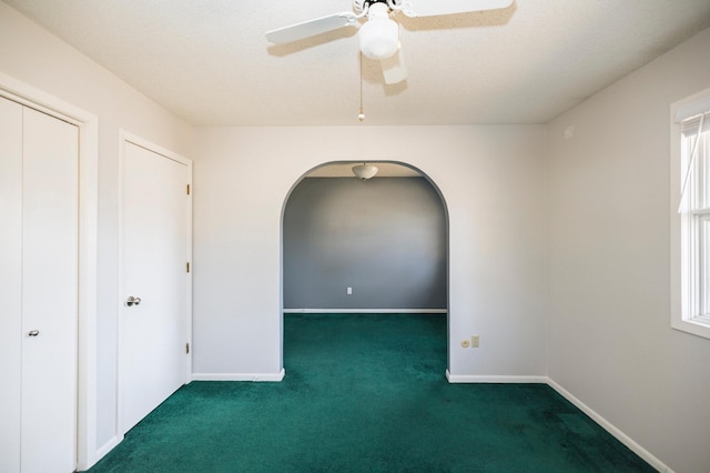 empty room featuring baseboards, arched walkways, carpet floors, and a ceiling fan