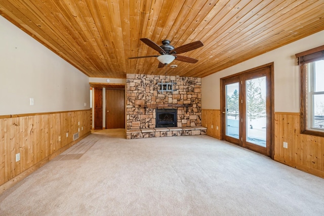 unfurnished living room with a stone fireplace, wood ceiling, wood walls, and wainscoting