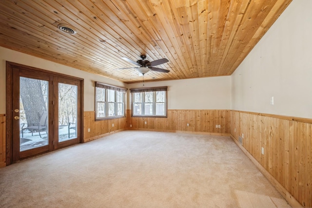 empty room with wooden walls, visible vents, wainscoting, wood ceiling, and light carpet