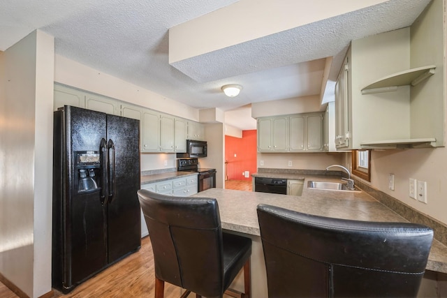 kitchen featuring a peninsula, a sink, black appliances, light wood-style floors, and a textured ceiling