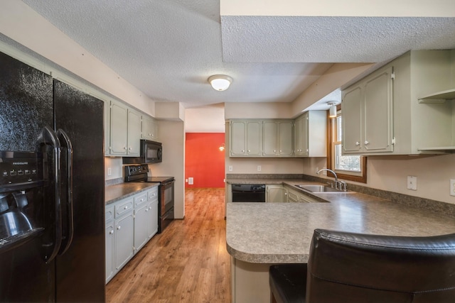 kitchen with light wood-type flooring, a peninsula, a textured ceiling, black appliances, and a sink