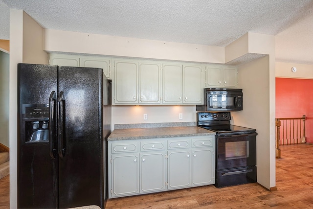 kitchen with light wood-type flooring, a textured ceiling, black appliances, and light countertops