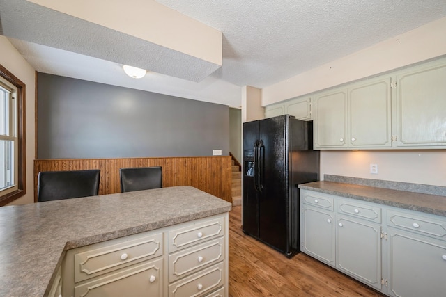 kitchen featuring black fridge with ice dispenser, light wood-style flooring, and a textured ceiling